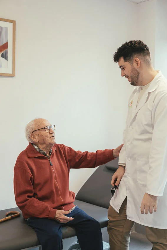 Hombre mayor sentado en una camilla siendo asistido por personal de la residencia
