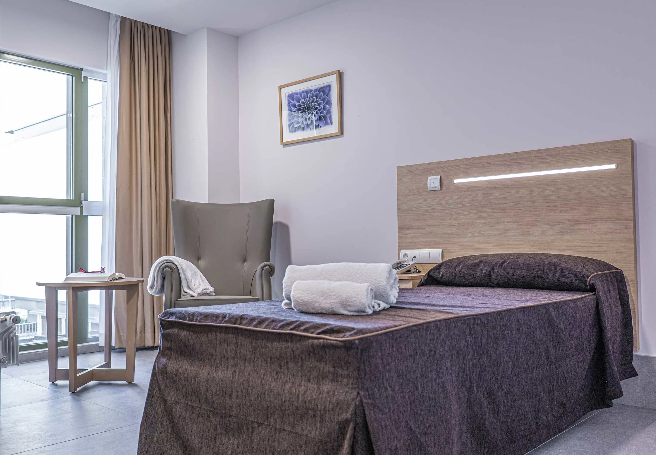 Cama, butaca y vista exterior de una habitación simple de la residencia Neurocare Home Mieses Valladolid